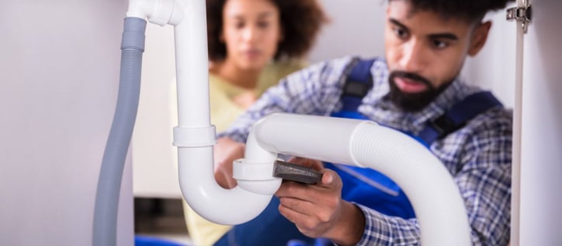 Close-up Of A Male Plumber Fixing Sink Pipe In Kitchen